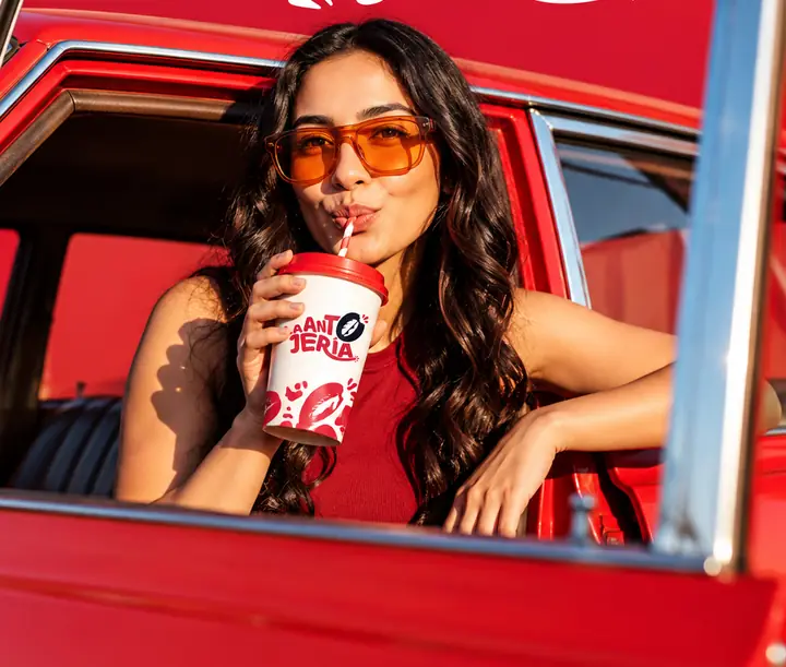 Chica tomando una bebida en vaso de La Antojería desde un auto rojo